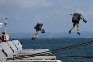 Two people in jet suits jump off an aircraft carrier