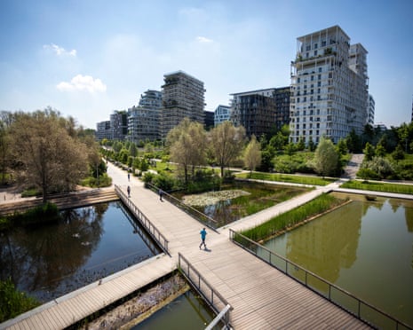 people walking along a boardwalk over ponds with buildings in the background