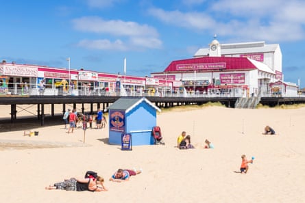 People on a sunny beach, with the pink and white Britannia pier behind