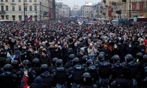 A very large crowd in a street in St.  Petersburg blocked the end of the room closest to the camera by a large continent riot police