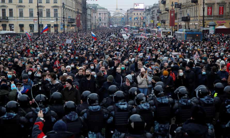 A very large crowd on a St Petersburg street blocked at the end nearest the camera by a large contingent of riot police