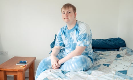 Callum McDonald, in a T-shirt and cotton leggings, sitting on a bed with a small table next to him, looking serious