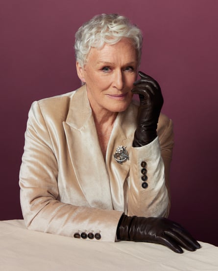 Glenn Close sitting at a round marble table, wearing a smart cream blazer and black leather gloves