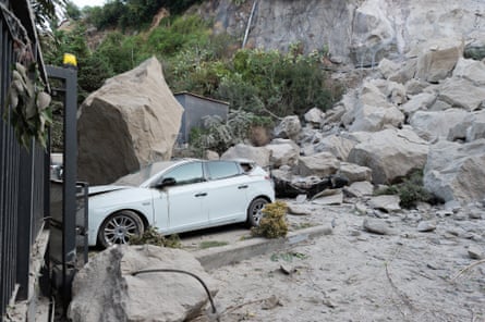 A car sits crushed under rocks outside a gate