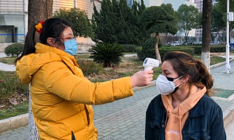 A woman uses a thermal imaging device to screen the temperatures of students at the entrance to Zhongnan University of Economics and Law in Wuhan.