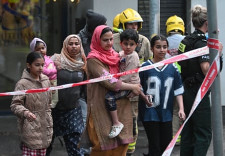 Police escort women and children past crime scene tape
