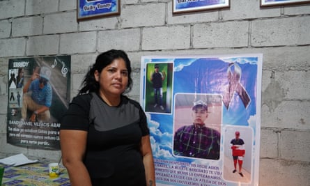 Maria Elena Villacís standing in front of a poster showing her deceased brothers at her home on the outskirts of Guayaquil, Ecuador