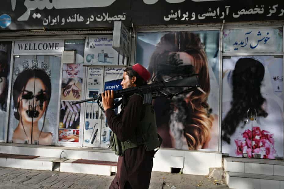 A Taliban fighter walks past a beauty salon with images of women defaced using spray paint in Shar-e-Naw in Kabul on August 18