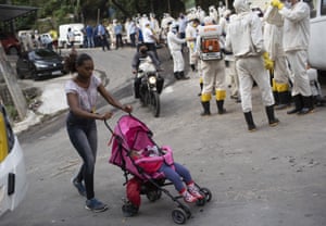 A woman walks past water utility workers will disinfect the Turano favela in an effort to curb the spread of the coronavirus in Rio.