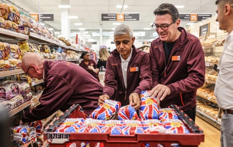 Burnham, Khan and McFadden dressed in Sainsbury’s fleeces stacking loaves of bread on to a shelf.