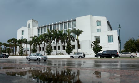 The outside of a large white building lined with palm trees and cars on the outside