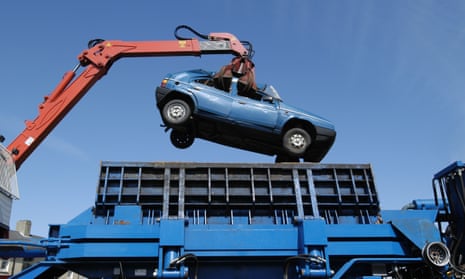 An old car being lowered into a car crusher by a crane, seen from below