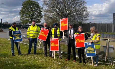 Members of the PCS union hold placards while standing on grass in front of a fence