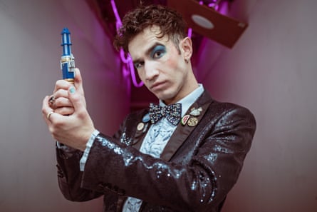 Heavily made up in a bow tie and jacket, he holds up a sonic screwdriver