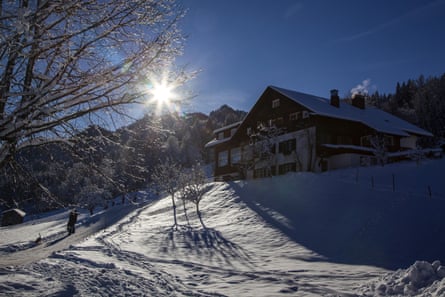 A chalet on a snowy hill with mountains behind on a sunny day