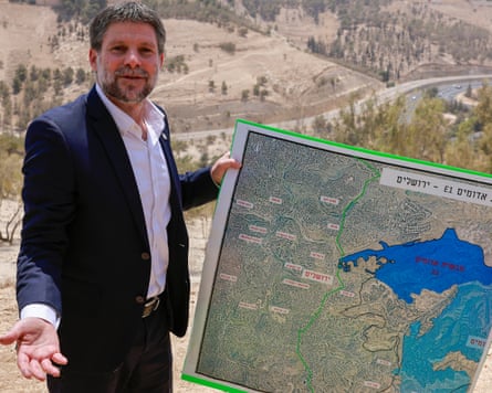 Israel’s finance minister Bezalel Smotrich in dark suit holding a map with proposed settlement zone.