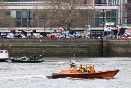 Police officers and the crew of an RNLI lifeboat patrol the Thames, with the counterprotest visible on the river-side street behind