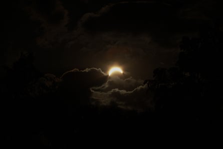 The eclipse in a dark sky, partly covered by clouds
