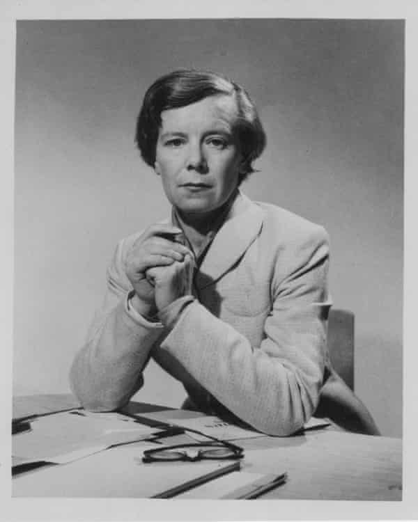 Alison Adburgham sits with her elbows on her desk and her hands clasped in front of her, looking directly at the camera, wearing a pale jacket buttoned up.