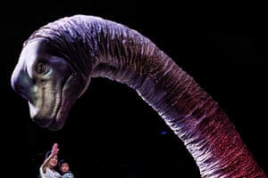 A woman and small child stand next to the giant neck and head of an animatronic Brachiosaurus