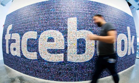 a Facebook employee walks past a Facebook sign