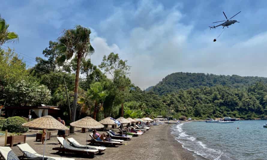 Sunbathers watch as a helicopter carries water from the sea to dump on fires near Marmaris.