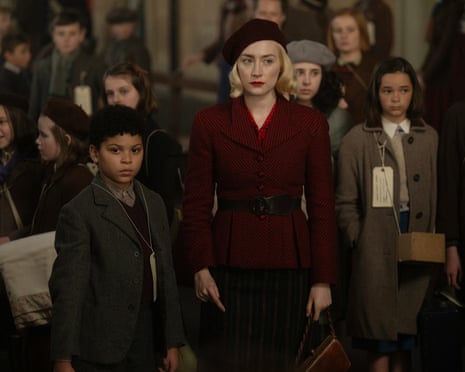 a boy and a woman in a red coat and hat stand in front of other children