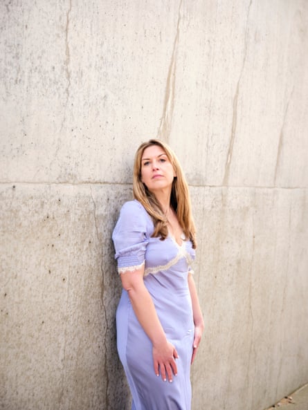 Daisy Buchanan standing outside wearing a lilac, lace-trimmed dress leaning against a concrete wall