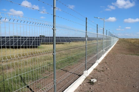 Banks of solar panels seen through a chain-link fence