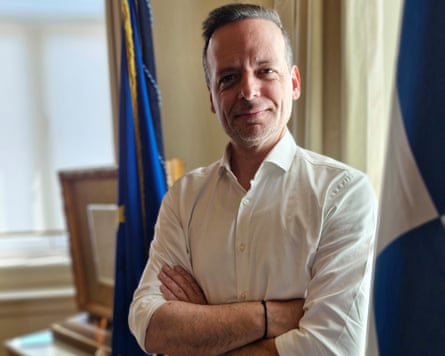 Haris Doukas standing between the Greek and European Union flags in his office.