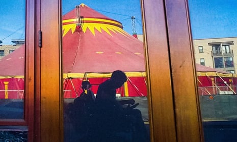 Reflection of a man in a wheelchair in a window with a circus tent behind him.