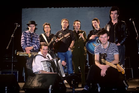 The eight men pose with their instruments for a photo in a music studio