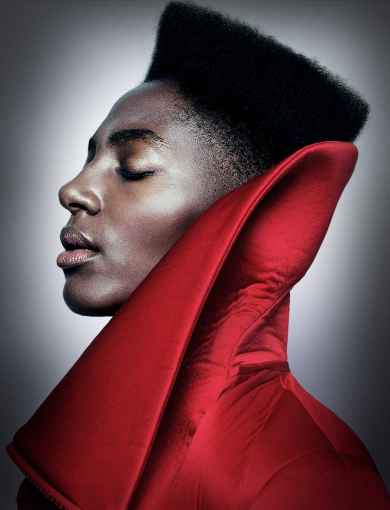 Head and shoulders of Ysra Daley-Ward in profile with her eyes closed wearing a red cloak with a large turned up collar