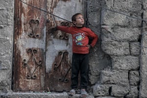 A Palestinian boy stands next to an old rusty door and looks up