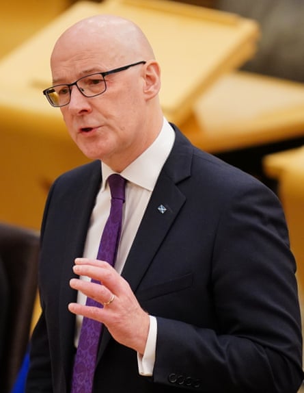 John Swinney stands speaking in dark suit and tie