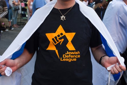 a man holds an Israeli emblem while wearing a garment that says ‘Jewish Defense League’