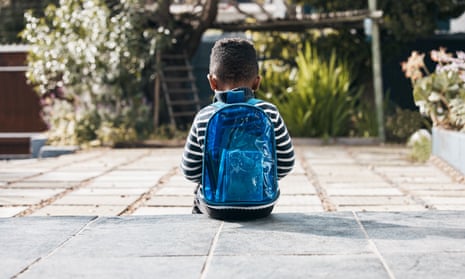 A young boy wearing a rucksack sits alone with his back to the camera.