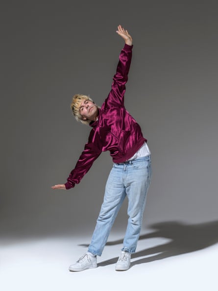 Tim Burgess in jeans and dark pink jacket, leaning to one side, arms outstretched, one up the other down