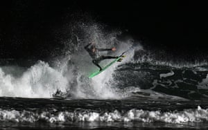 A surfer rides his board at an angle above the water as waves crash next to him