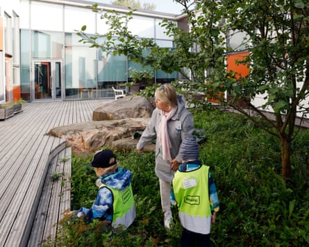 A woman and two children in hi-vis vests stand under a tree in a courtyard
