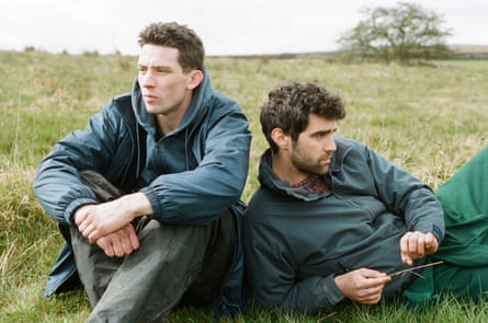 Josh O’Connor and Alec Secareanu sitting on a grassy hill
