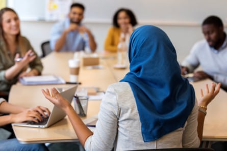 Back view of a woman in a hijab speaking to a table of colleagues