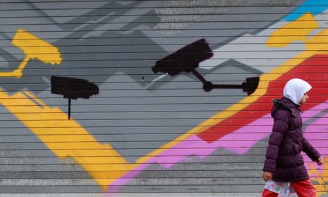 A girl walks past graffiti showing CCTV cameras in the Sparkbrook area of Birmingham, England