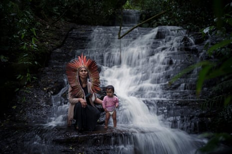 Mujer con un tocado con un bebé en pañales junto a una cascada.