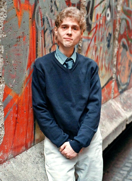 David Reimer in ablue jumper leans against a wall covered in graffiti