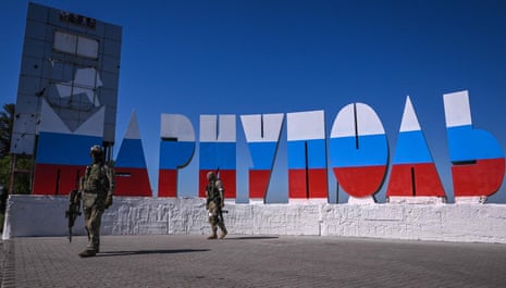 Russian servicemen walk near the welcome sign Mariupol, which has been painted in Russian flag colours, at the entrance of the city