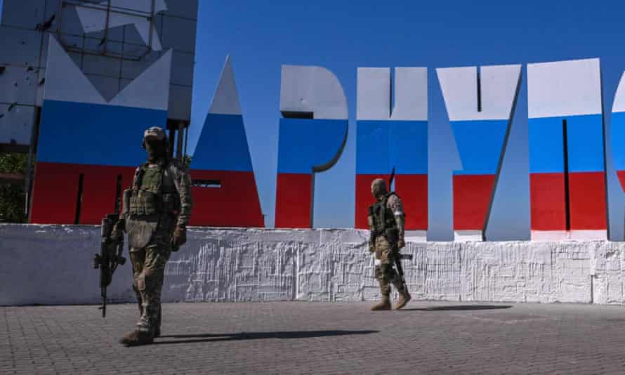 Russian servicemen walk near the welcome sign in Mariupol, which has been painted in Russian flag colours