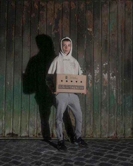 Leonardo, a young volunteer, holds a box used for rescuing birds, standing before a wooden door