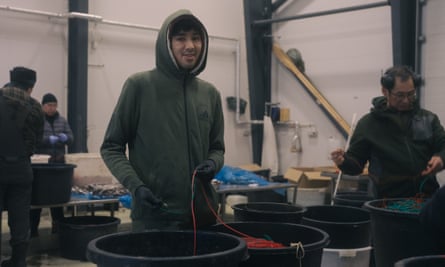 Man with hood looks at camera with several othrs around working in white interior