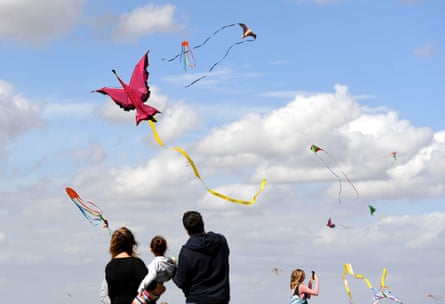 A family flies a flamingo kite on a sunny day with lots of other kites in the sky